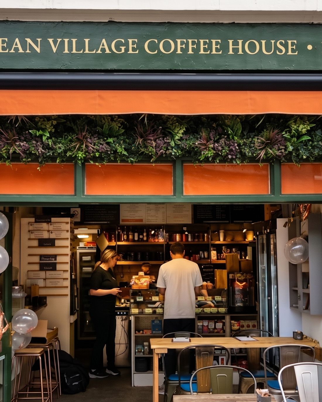 Dean Village Coffee House at 54 Belford Road: a green shopfront under an orange awning, the doors folded back onto tables and stools on the pavement.
